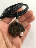 Ammonite fossil pendant on a black cord held in a hand against a white background