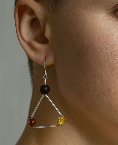 Close-up of an ear wearing a triangle-shaped earring with amber beads.