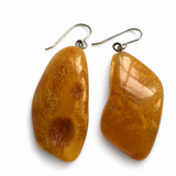 A pair of handmade dangle earrings featuring polished, irregular-shaped amber stones with silver fishhook wires, displayed on a clean white background.
