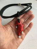 Red irregular-shaped coral pendant with a black cord held in a hand on a light background