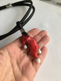 Hand holding a red organic-shaped coral pendant with pearls on a black cord against a white background