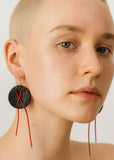 Close-up of a person wearing a unique earring with a black circular design and red strings.