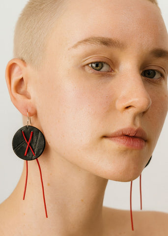 Close-up of a person wearing a unique earring with a black circular design and red strings.