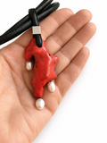 Red coral organic-shaped pendant with pearls on a black cord held in a hand against a white background